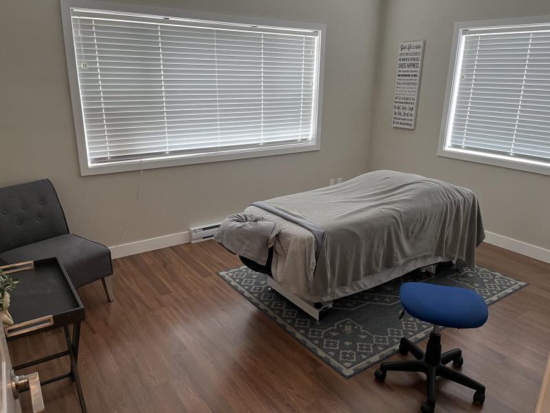 Massage table beside two windows, with a chair and wooden flooring in the Duncan clinic