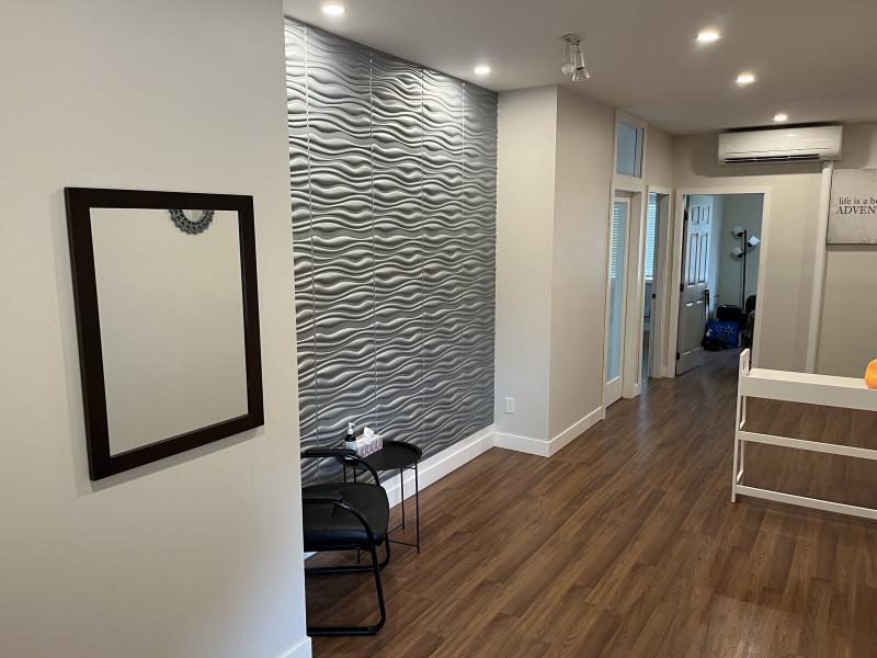 Clinic reception area with seating, a mirror and a textured wall beside the hallway