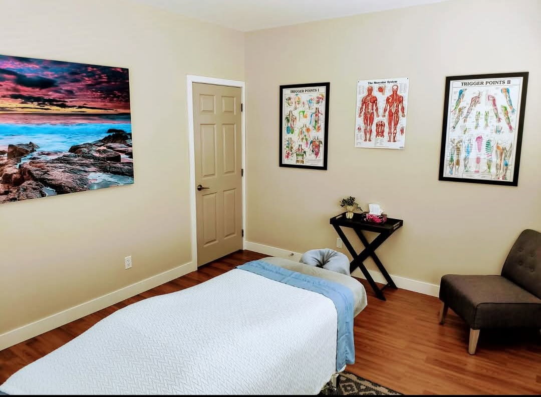 Massage treatment room at TK Registered Massage Therapy in Duncan, with a covered table, coastal artwork and anatomy charts